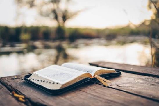 An open Bible on a wooden dock by the water