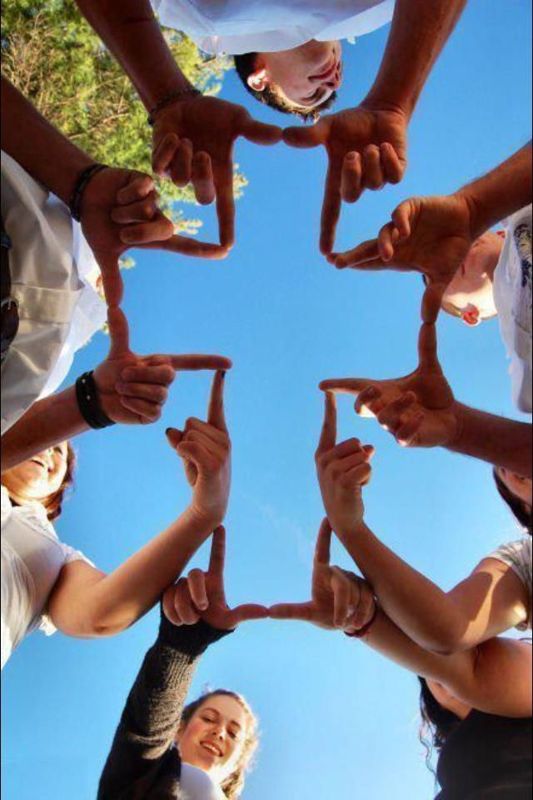 Friends joining hands to form a cross against a blue sky