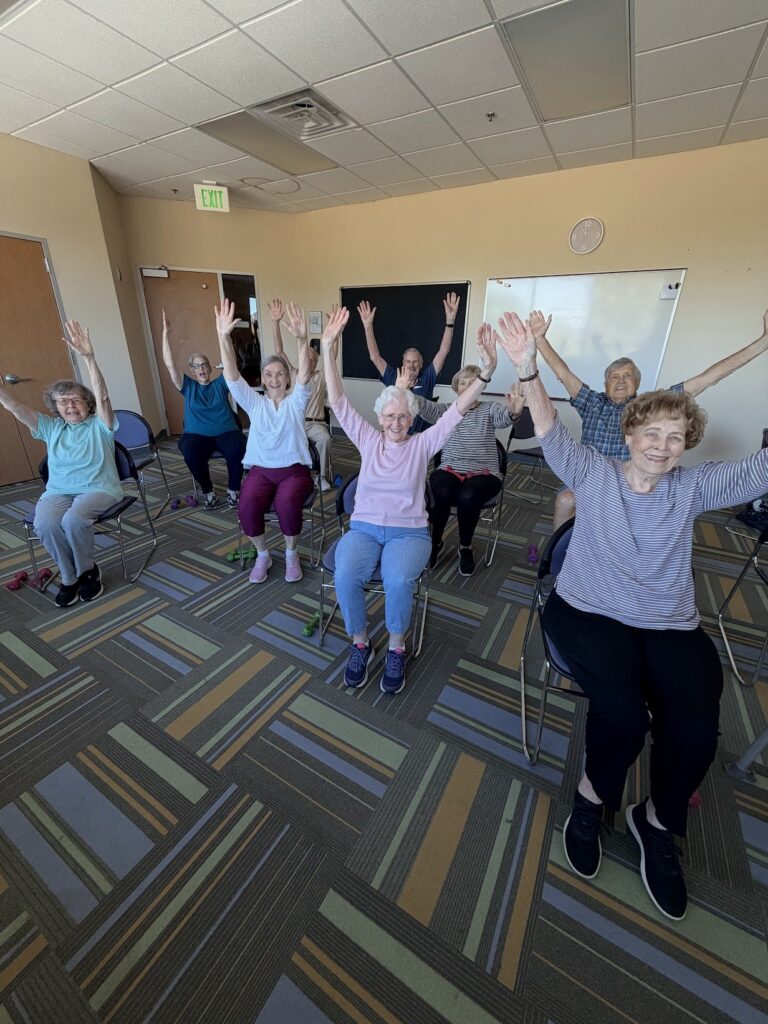 Seniors raising their arms and smiling during a chair exercise class at Mission Lutheran Church